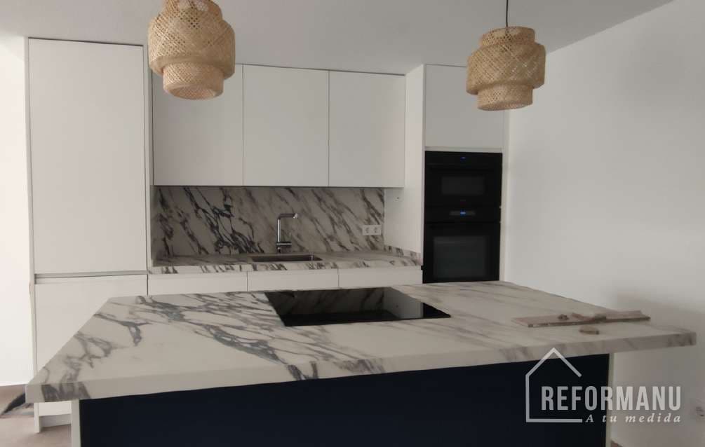 Kitchen renovated by REFORMANU in Elche: island and marble worktop, white fronts and designer lighting